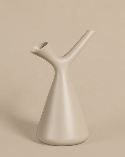 Eine minimalistische beige Vase mit einzigartigem Design mit zwei Ausgüssen, von denen einer nach oben und der andere leicht nach unten gerichtet ist. Die Plunge Giesskanne aus Polypropylen hat eine glatte, moderne Oberfläche und einen konischen Sockel, der sich elegant in den Hintergrund einfügt.