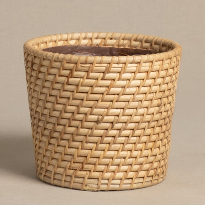 Der Calen Pflanzenkorb aus Rattan (14cm Ø) ist ein runder, handgeflochtener Korb in hellen Naturtönen mit sichtbarer Kunststoffeinlage, abgebildet auf schlichtem beigem Untergrund.