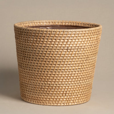 Der Pflanzenkorb aus Rattan (Calen | 22cm Ø) ist ein runder, hellbrauner handgefertigter Korb mit glattem Innenfutter, abgebildet auf einem schlichten beigen Hintergrund.