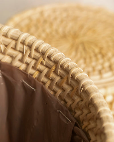 Nahaufnahme des Pflanzenkorbs aus Rattan (Calen | 25 cm Ø) mit einem braunen Kunststoffeinsatz im Inneren. Das detaillierte rattanähnliche Geflecht und die Textur sind sichtbar, während ein weiteres geflochtenes Element im Hintergrund leicht verschwommen ist.