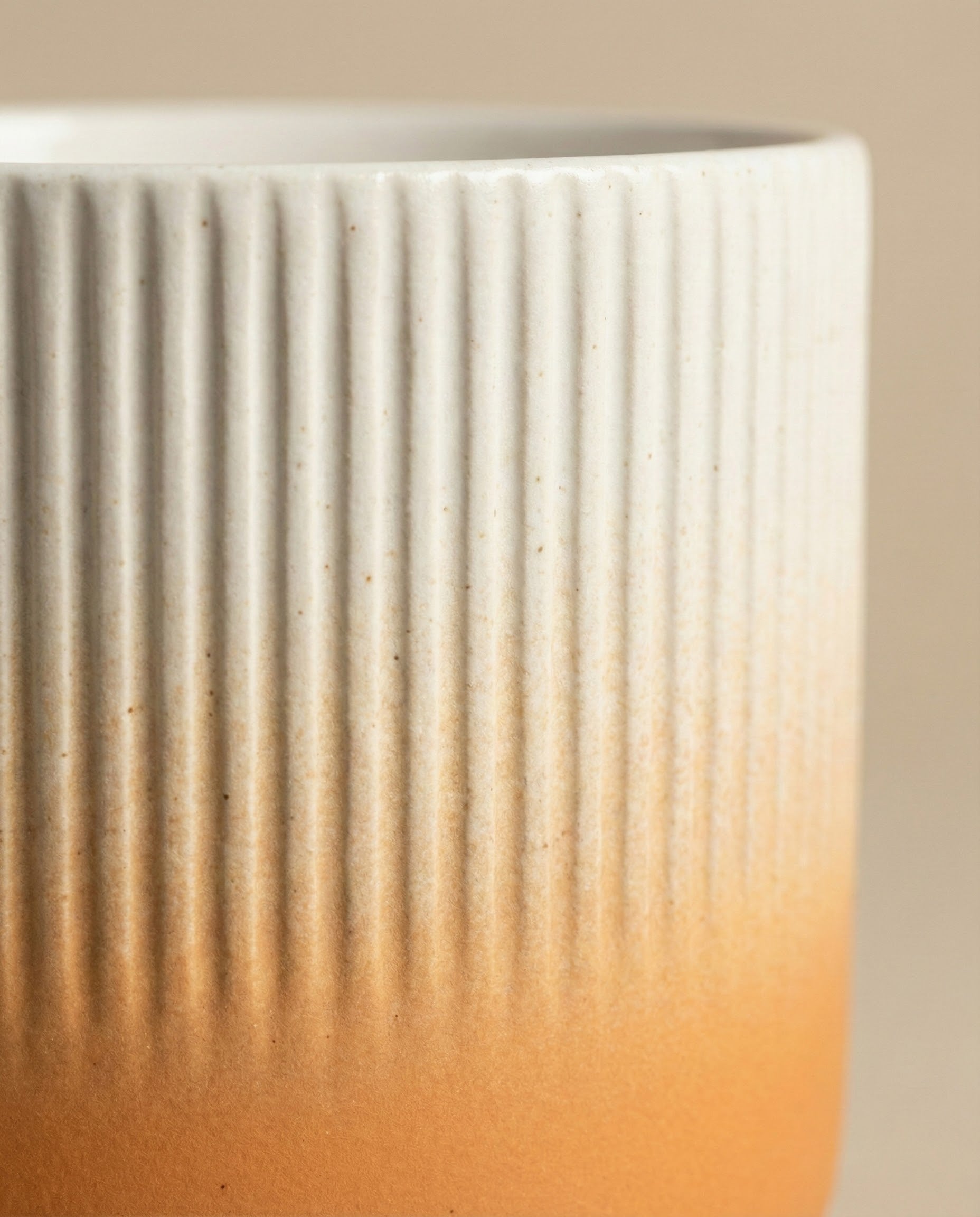 Nahaufnahme des Keramik-Topfes (Rilio | 14 cm ø) mit vertikaler Rippenstruktur und sanftem Farbverlauf von Weiß am oberen Rand zu warmem Orange am unteren Rand, vor einem schlichten, neutralen Hintergrund.