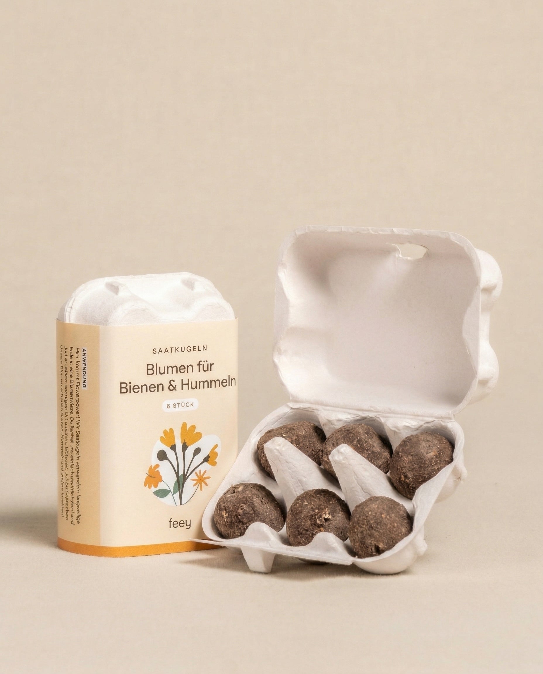 Ein kleiner offener Karton enthält sechs Saatkugeln für Feld- & Wiesenblumen neben einer Schachtel mit 