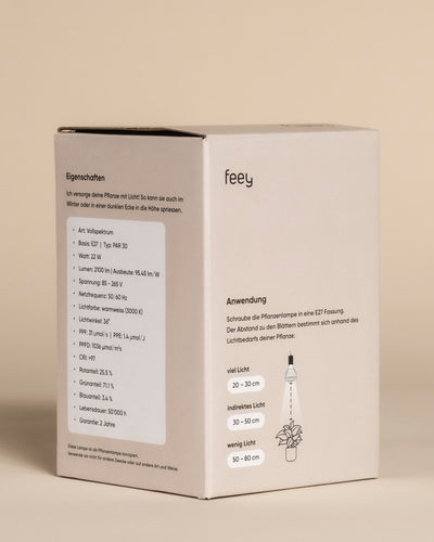 Der Produktkarton der Pflanzenlampe 'Staila' zeigt auf der linken Seite die technischen Daten in deutscher Sprache und auf der rechten Seite eine anschauliche Illustration, die die optimale Platzierung der Lampe für das Sonnenlicht der Zimmerpflanzen demonstriert.