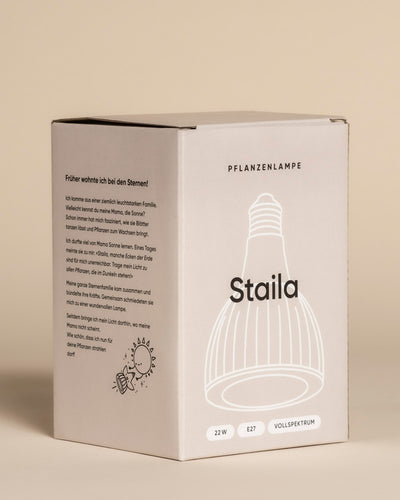 Die beigefarbene Schachtel der Pflanzenlampe 'Staila' zeigt eine Glühbirne und die Aufschrift "PFLANZENLAMPE" mit 22W, E27, Vollspektrum - ideal als Sonnenlicht-Ersatz für Zimmerpflanzen. Die Seitenwände enthalten deutschen Text und einfache Grafiken.