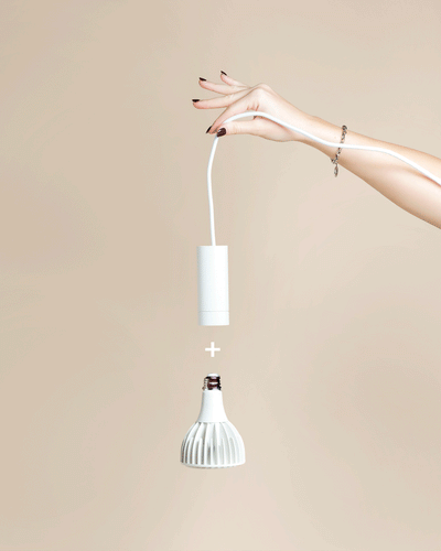 Eine Hand mit lackierten Nägeln hält eine weiße Pendelleuchte 'Corda' über einer passenden weißen LED-Glühbirne, die mit einem Pluszeichen dazwischen abgebildet ist - perfekt für eine stilvolle Beleuchtung von Zimmerpflanzen vor einem beigen Hintergrund.