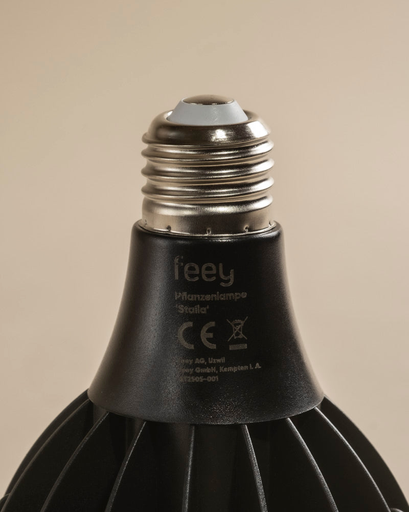 Nahaufnahme des Schraubsockels und des oberen Teils einer schwarzen LED-Pflanzenlampe mit der Aufschrift "feey Pflanzenlampe Staila" mit CE-Kennzeichnung und Herstellerangaben, ideal für Zimmerpflanzen, vor einem schlichten beigen Hintergrund.