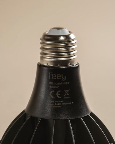 Nahaufnahme des Schraubsockels und des oberen Teils einer schwarzen LED-Pflanzenlampe mit der Aufschrift "feey Pflanzenlampe Staila" mit CE-Kennzeichnung und Herstellerangaben, ideal für Zimmerpflanzen, vor einem schlichten beigen Hintergrund.