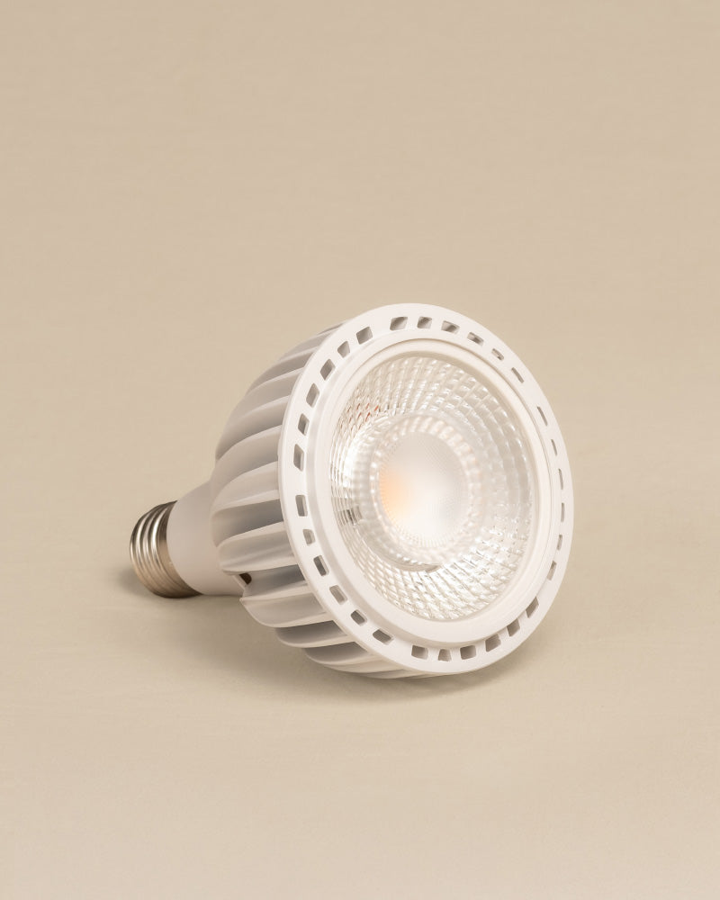 Die Pflanzenlampe 'Staila' ist eine weiße LED-Strahlerlampe mit geriffeltem Gehäuse und metallischem Schraubsockel, die seitlich vor einem hellbeigen Hintergrund abgebildet ist - perfekt, um Ihre Zimmerpflanzen mit Sonnenlicht zu versorgen und gesund zu halten.