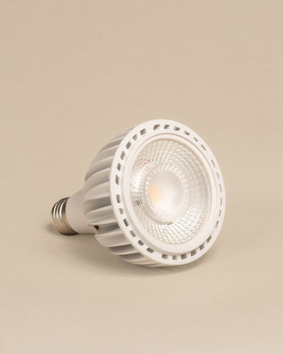 Die Pflanzenlampe 'Staila' ist eine weiße LED-Strahlerlampe mit geriffeltem Gehäuse und metallischem Schraubsockel, die seitlich vor einem hellbeigen Hintergrund abgebildet ist - perfekt, um Ihre Zimmerpflanzen mit Sonnenlicht zu versorgen und gesund zu halten.