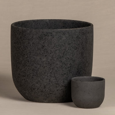 Bild von zwei schwarzen, steinähnlichen, zylindrischen Keramik-Topfsets 'Direito' (18, 7) unterschiedlicher Größe, nebeneinander vor einem neutralen Hintergrund platziert. Der größere Topf steht links hinter dem kleineren, beide weisen eine glatte, gesprenkelte Textur mit einem bunten Touch auf.