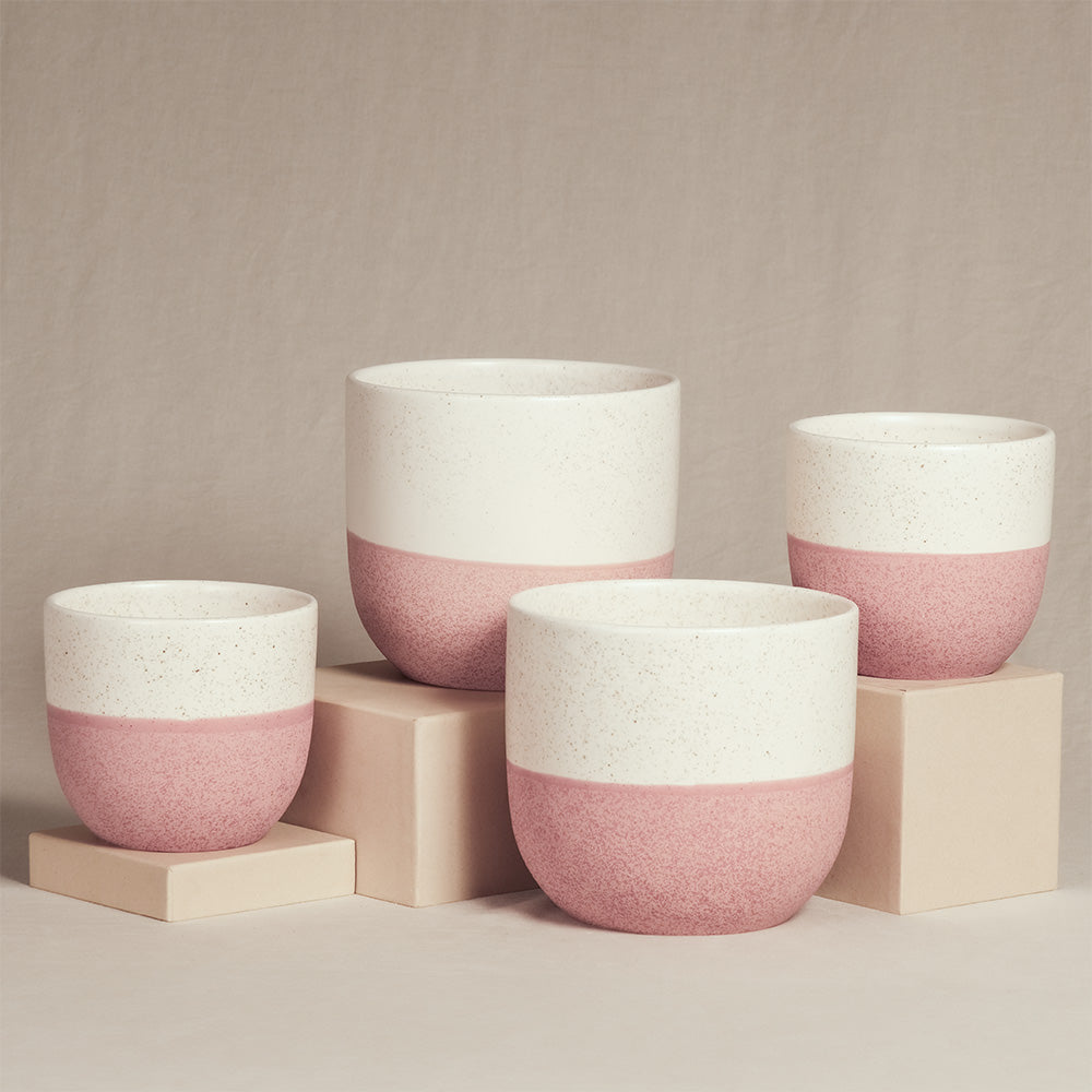 Vier Keramik-Topfsets „Variado“ (2 × 18, 2 × 14) in unterschiedlichen Größen sind auf beigen Würfeln vor neutralem Hintergrund ausgestellt. Die Innentöpfe sind zweifarbig gestaltet, mit einer rosa gesprenkelten unteren Hälfte und einer weißen oberen Hälfte.