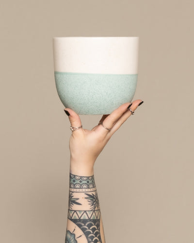 Hand streckt einen mintfarbigen feey Keramik-Topf Variado in die Höhe