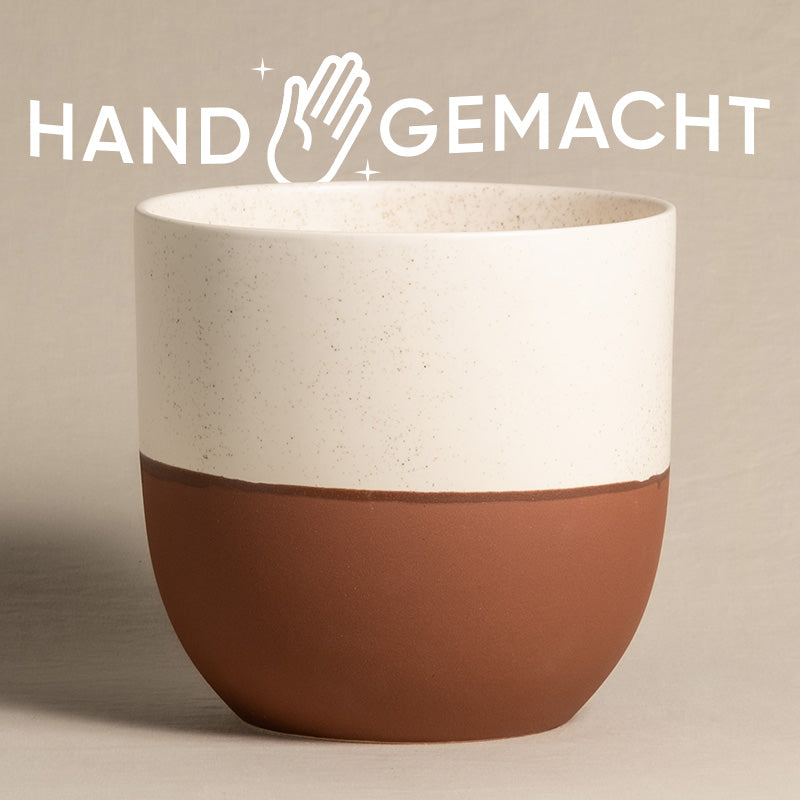 Abgebildet ist ein toller Keramik-Topf (Variado | 22 cm ⌀) aus unserer bunten Topfkollektion, der eine weiß gesprenkelte obere Hälfte und eine strukturierte, rötlich-braune untere Hälfte aufweist. Über dem Keramiktopf steht in weißen Großbuchstaben das Wort „HANDGEMACHT“ mit einem Handsymbol zwischen „HAND“ und „GEMACHT“.