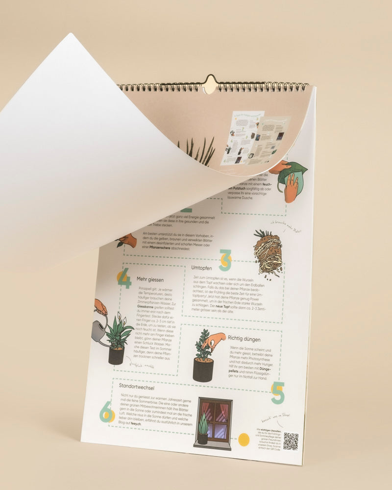 Ein offener, spiralgebundener Pflanzenkalender zeigt illustrierte Pflanzentipps für Zimmerpflanzen - nummerierte Abschnitte mit Zeichnungen von Händen, Pflanzen und Töpfen auf einem beigen Hintergrund. Eine Seite des immerwährenden Kalenders ist teilweise umgeschlagen.