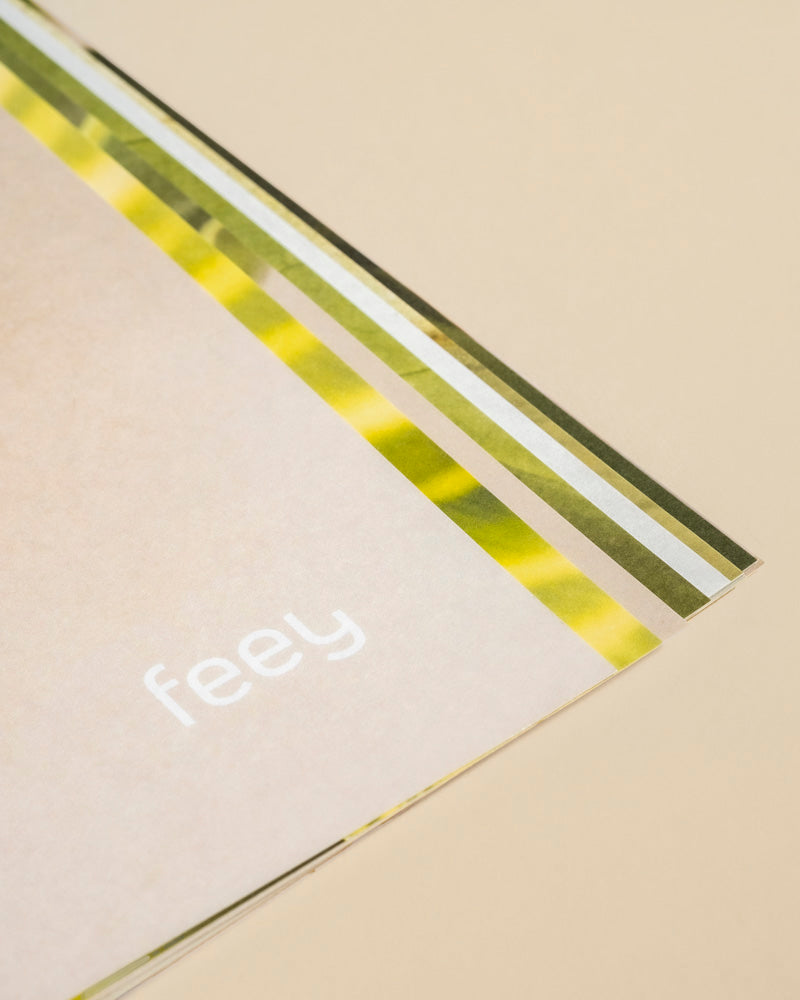 Eine Nahaufnahme einer beige-grün gestreiften Pflanzenkalenderkarte auf hellem Untergrund, mit "feey" in weißer Unterschrift - ideal für Zimmerpflanzen-Fans auf der Suche nach stilvollen Pflanzentipps oder einem einzigartigen immerwährenden Kalender.
