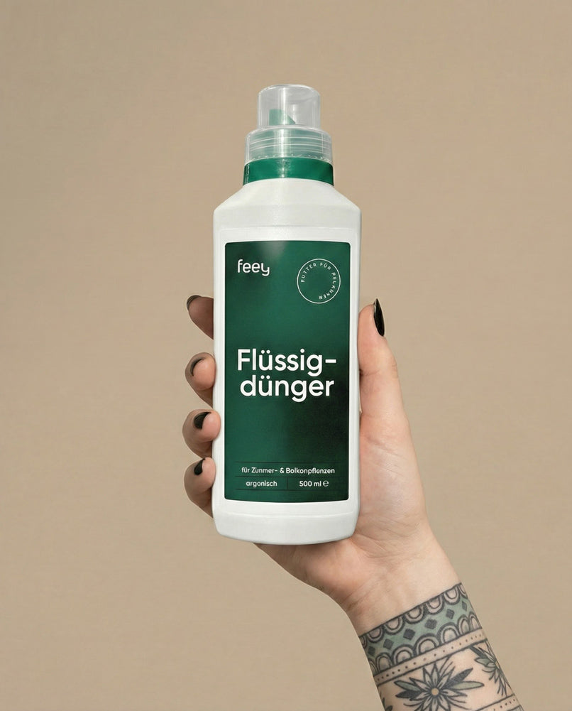 Eine Hand mit schwarzem Nagellack und einer Tätowierung hält eine weiße Flasche mit der Aufschrift 