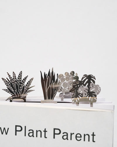 Buchzeichen aus Stahl in Form einer Calathea, Sansevieria, Pilea und Monstera in einem Plant Parent Buch