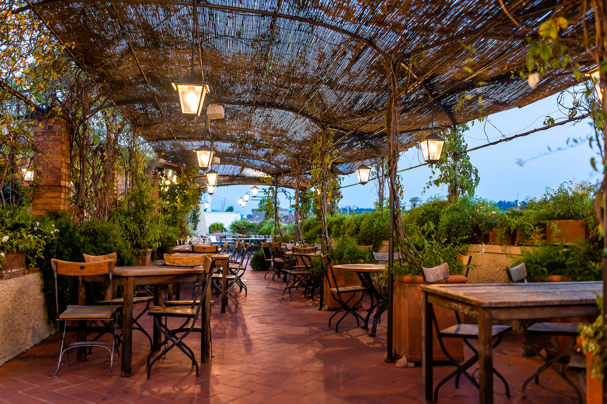 Gemütliches, rustikal eingerichtetes Terrassenrestaurant mit Pergola, an deren Stützen Kübelpflanzen emporklettern.