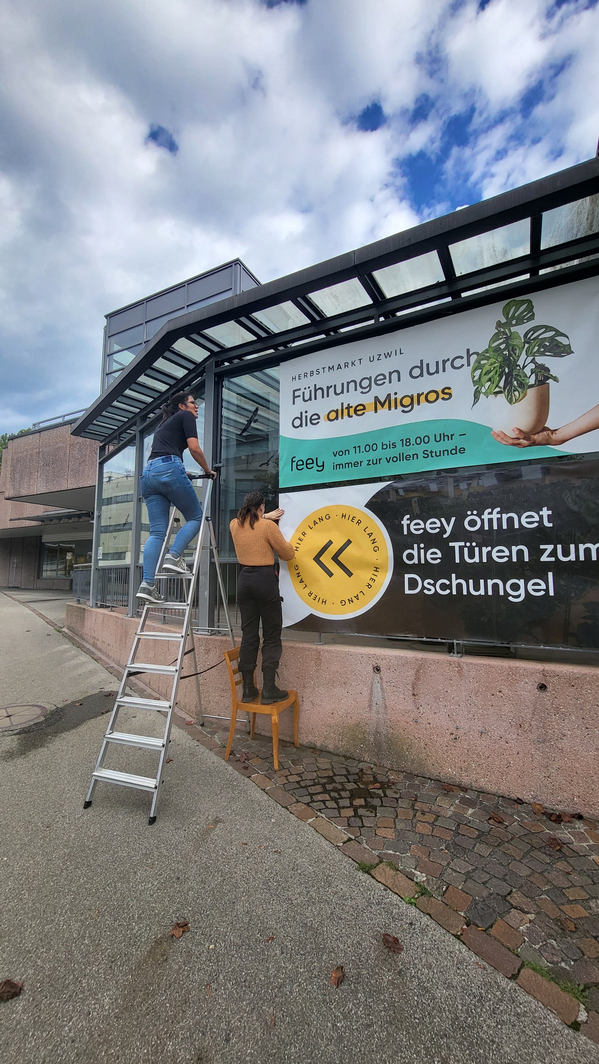 Zwei Personen bringen Plakate an einer Fensterscheibe an.