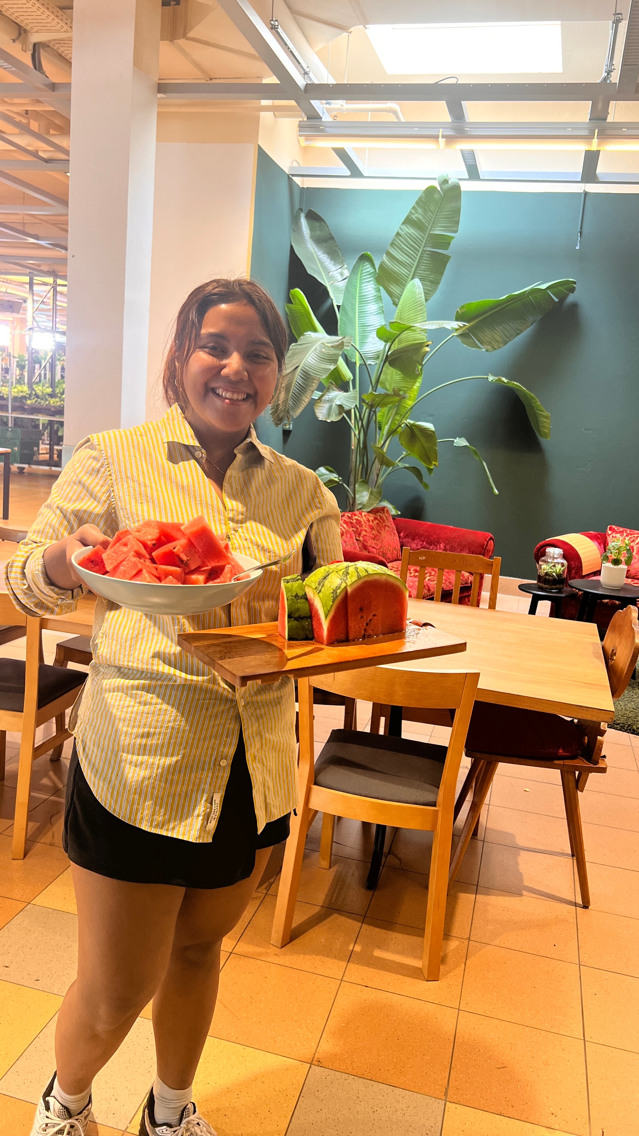 Eine Frau hält geschnittene Wassermelone auf Teller und Schneidebrett in den Händen.