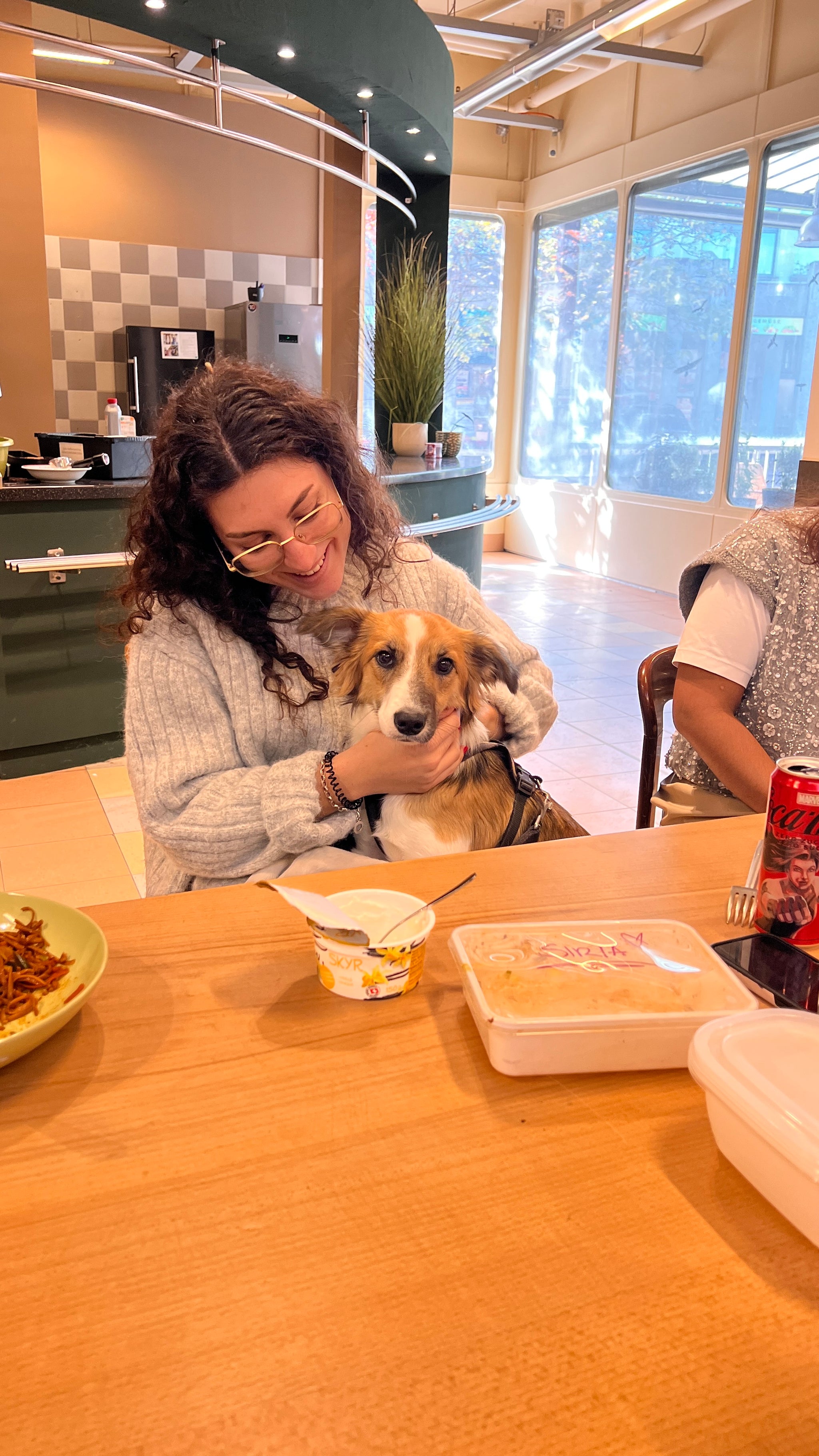 Ein Hund sitzt zusammen mit einer Frau am Esstisch.