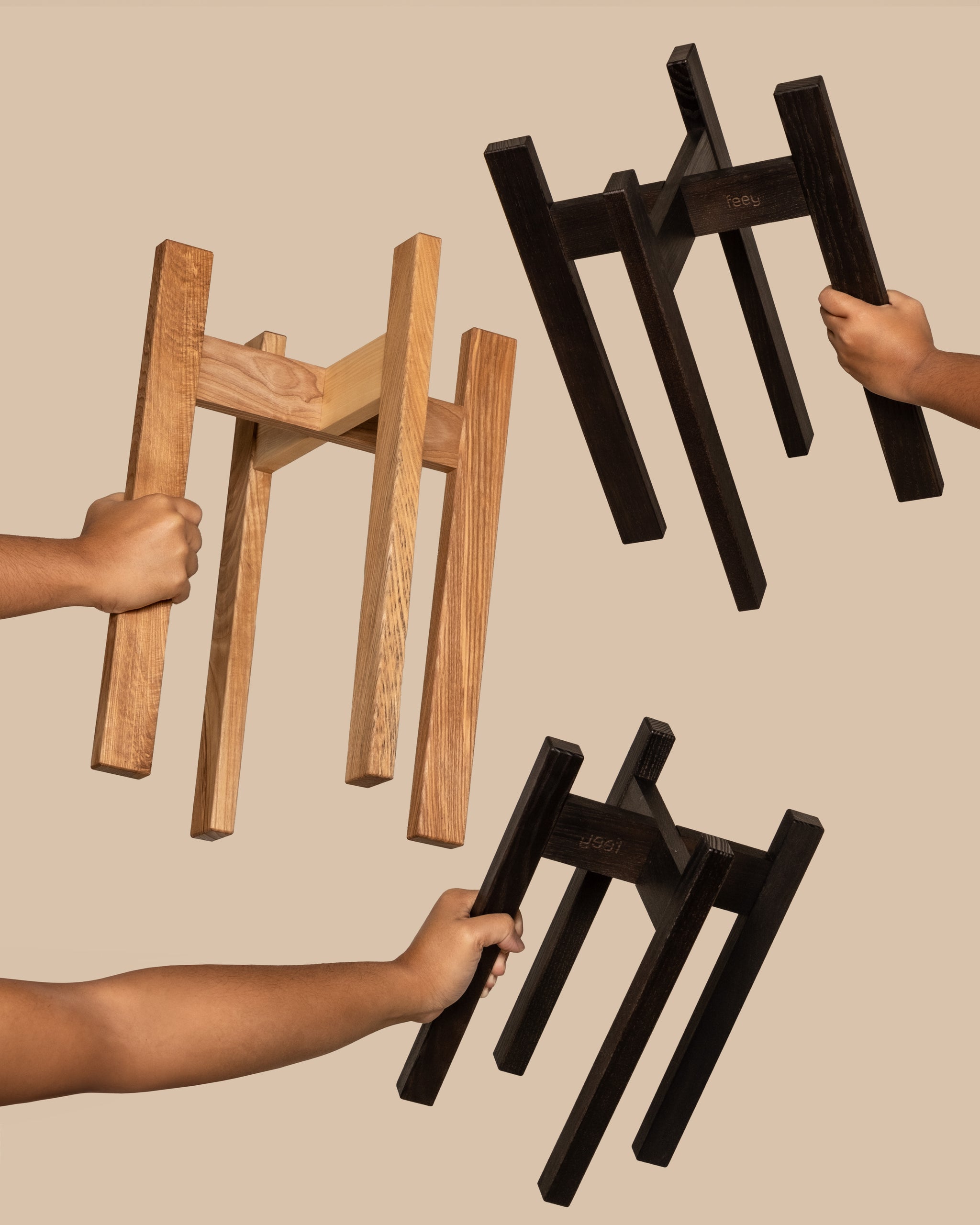 Drei Pflanzenständer ‘Stelion’ in schwarz oder ohne Lack aus Holz werden von je einer Hand gehalten.