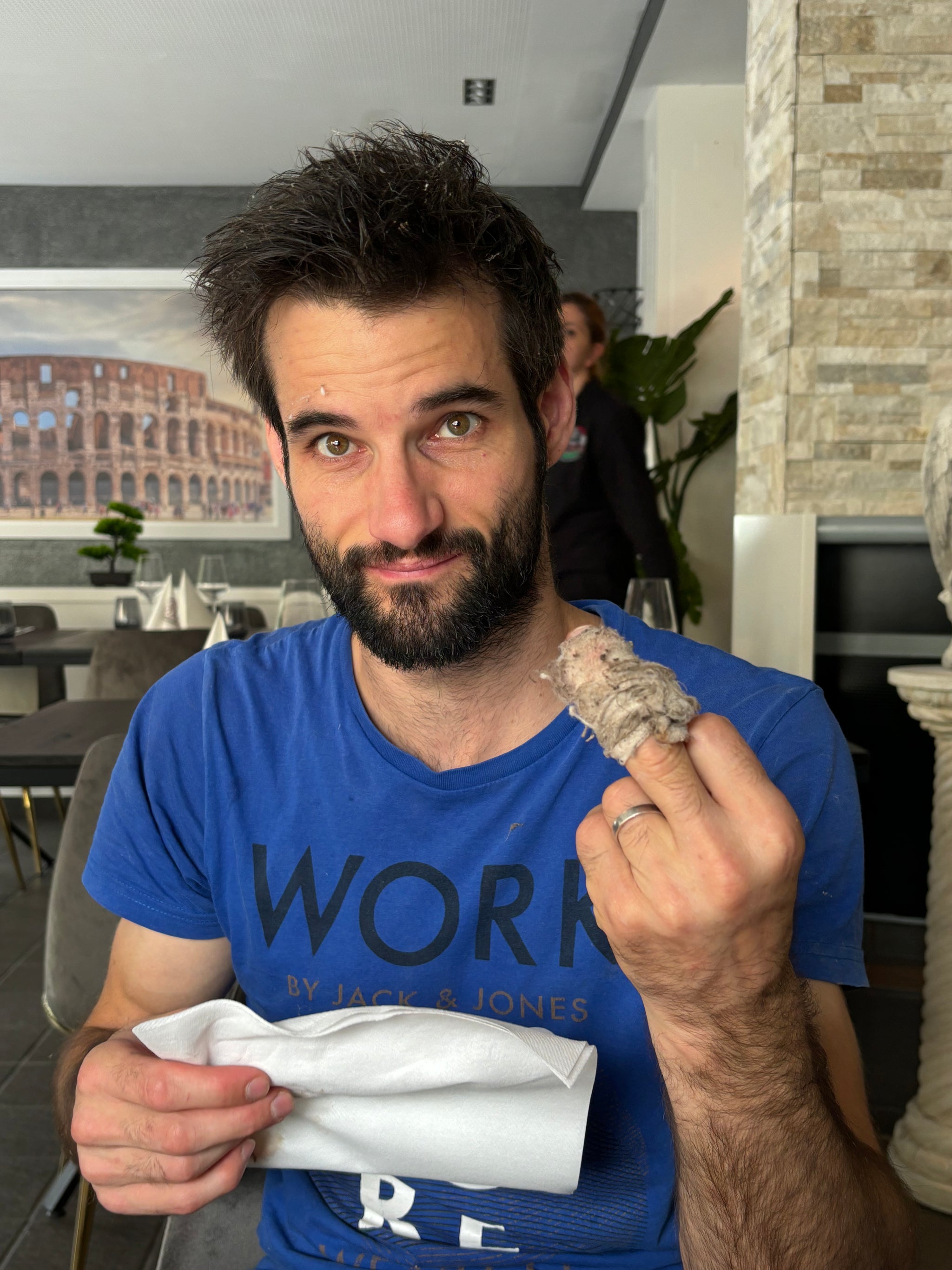 Mann in einem blauen T-Shirt mit einem umwickelten, verletzten Mittelfinger.