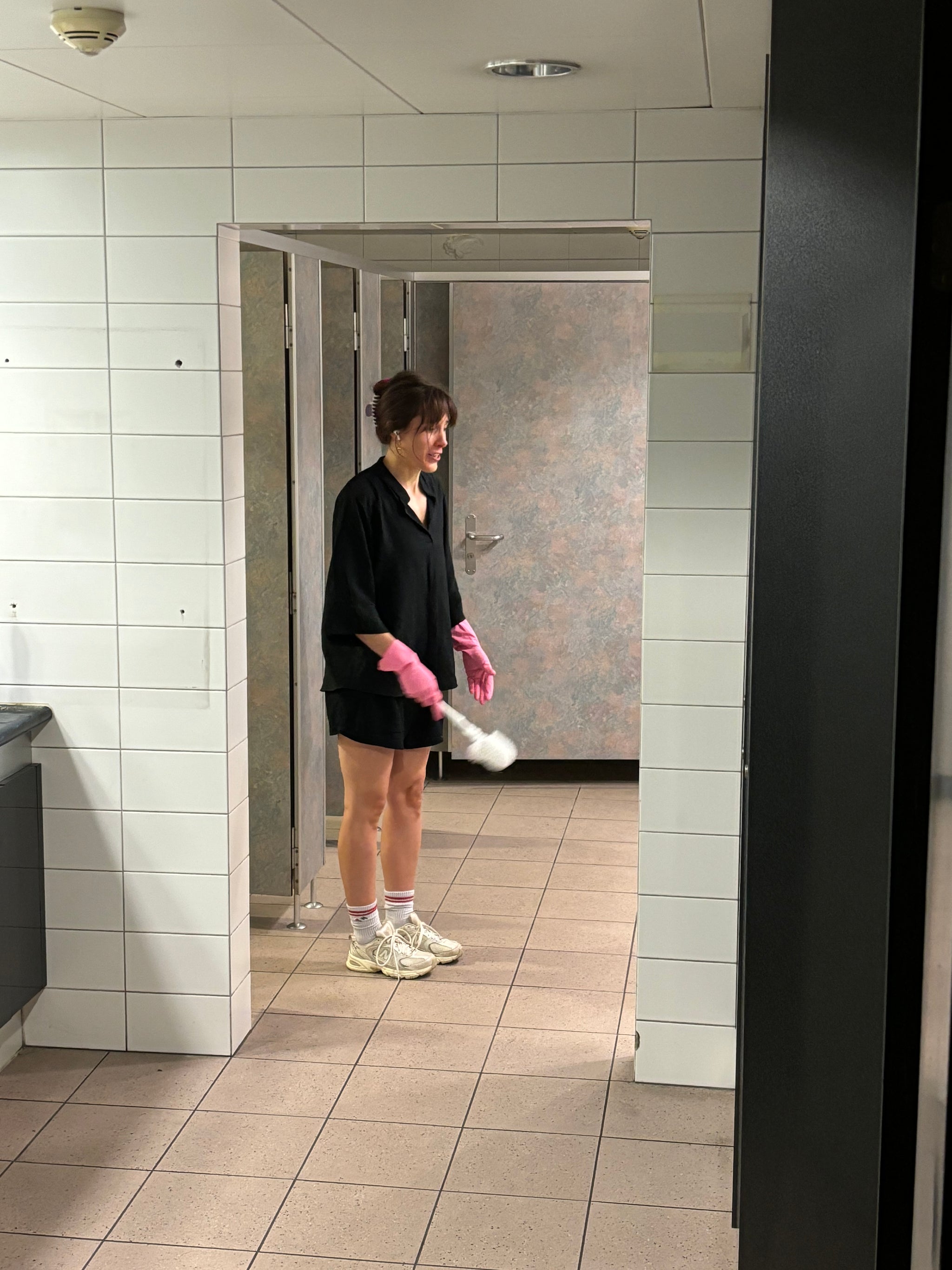 Eine Frau mit WC-Bürste steht in einem Türrahmen.