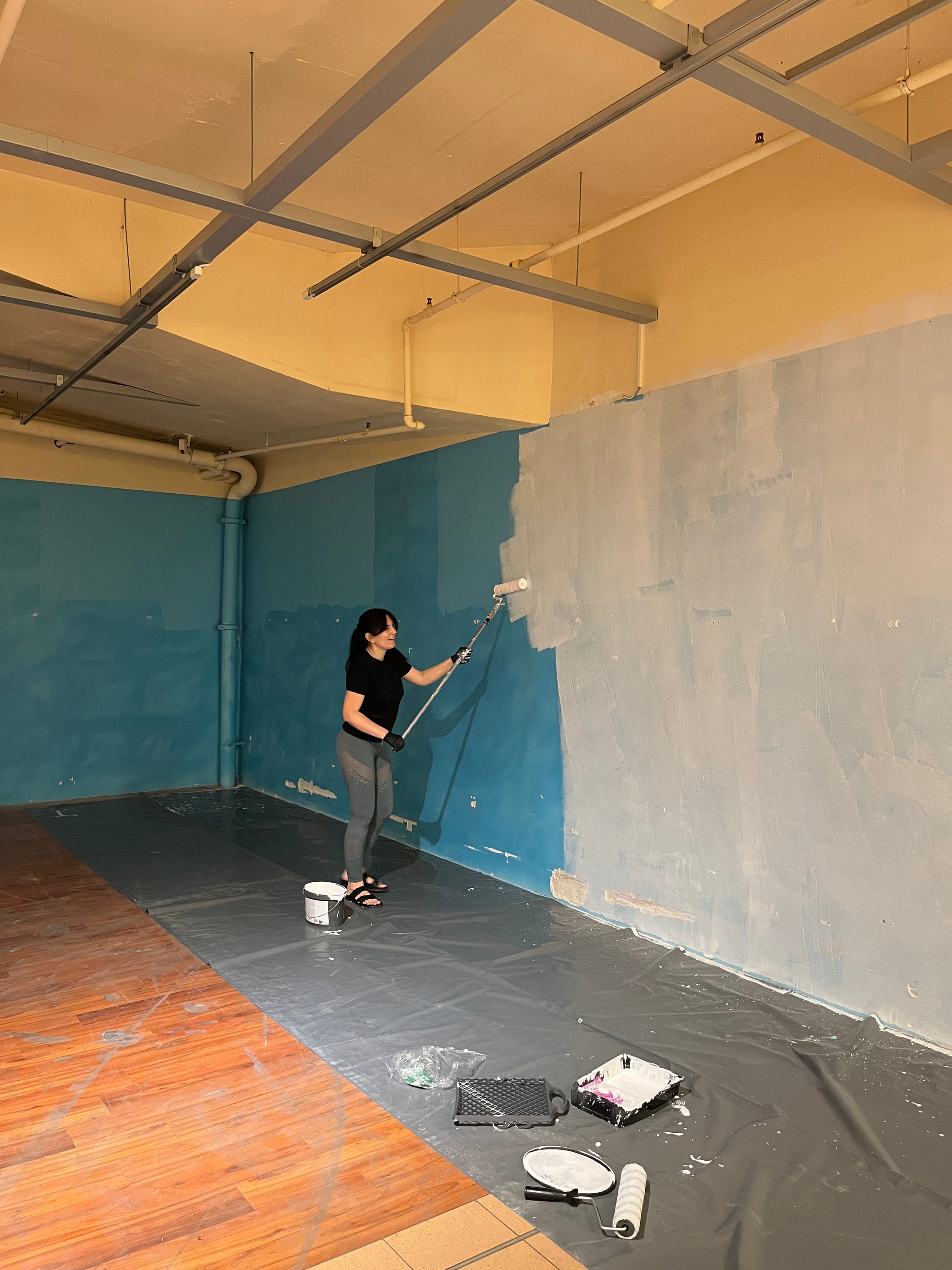 Eine Person überstreicht eine blaue Wand mit weisser Farbe.