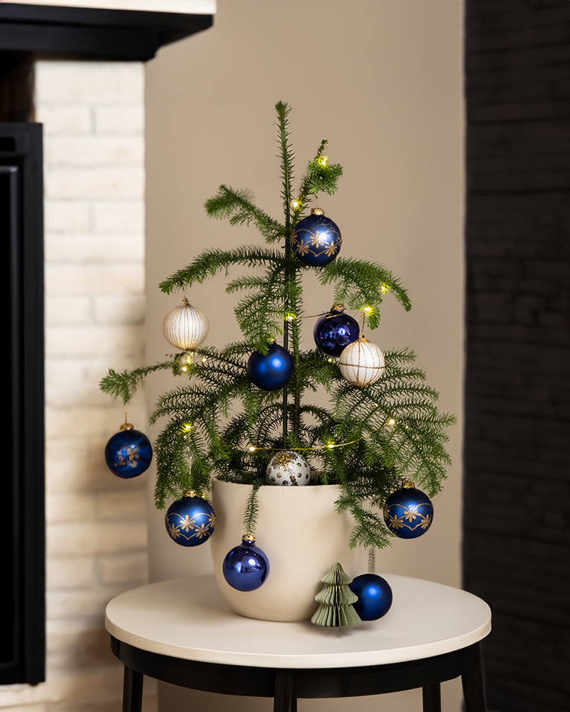 Eine als Weihnachtsbaum geschmückte Zimmertanne steht auf einem Beistelltisch neben dem Kamin.