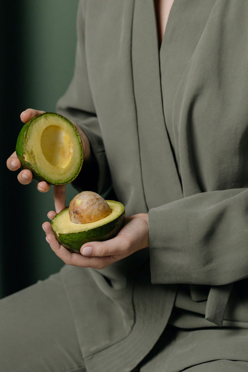 Eine Person in olivgrüner Kleidung hält in jeder Hand eine Avocadohälfte
