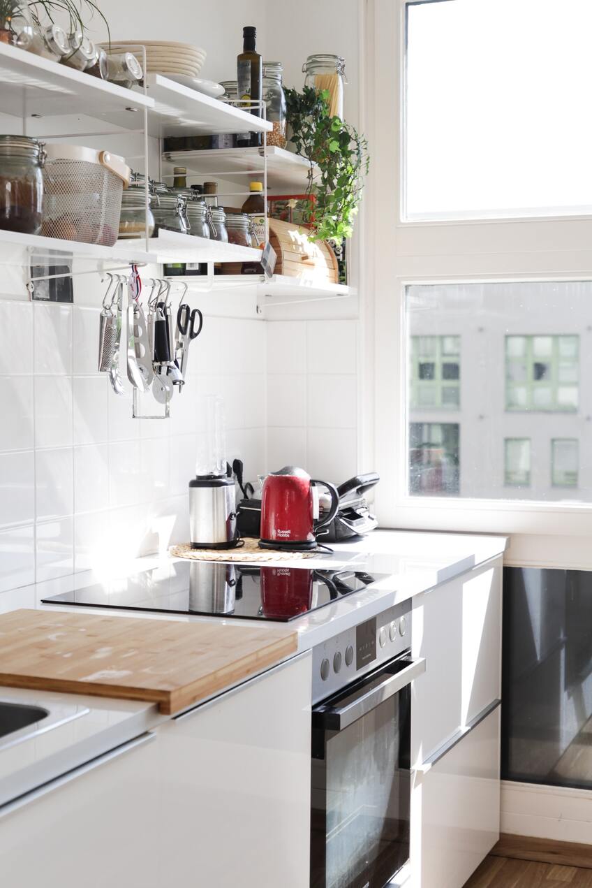 Weisse Küche mit einem roten Wasserkocher und einem weissen Wandregal, aus dem ein Efeu lugt