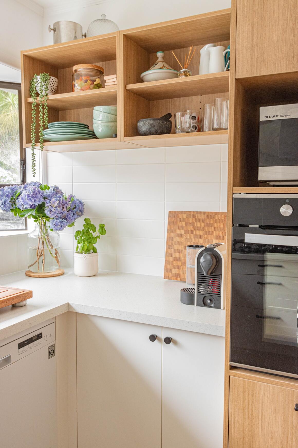 Weiss-hölzerne Küche mit einer kleinen Pflanze in der Ecke der weissen Arbeitsfläche und einem Strauss Blumen am selben Ort