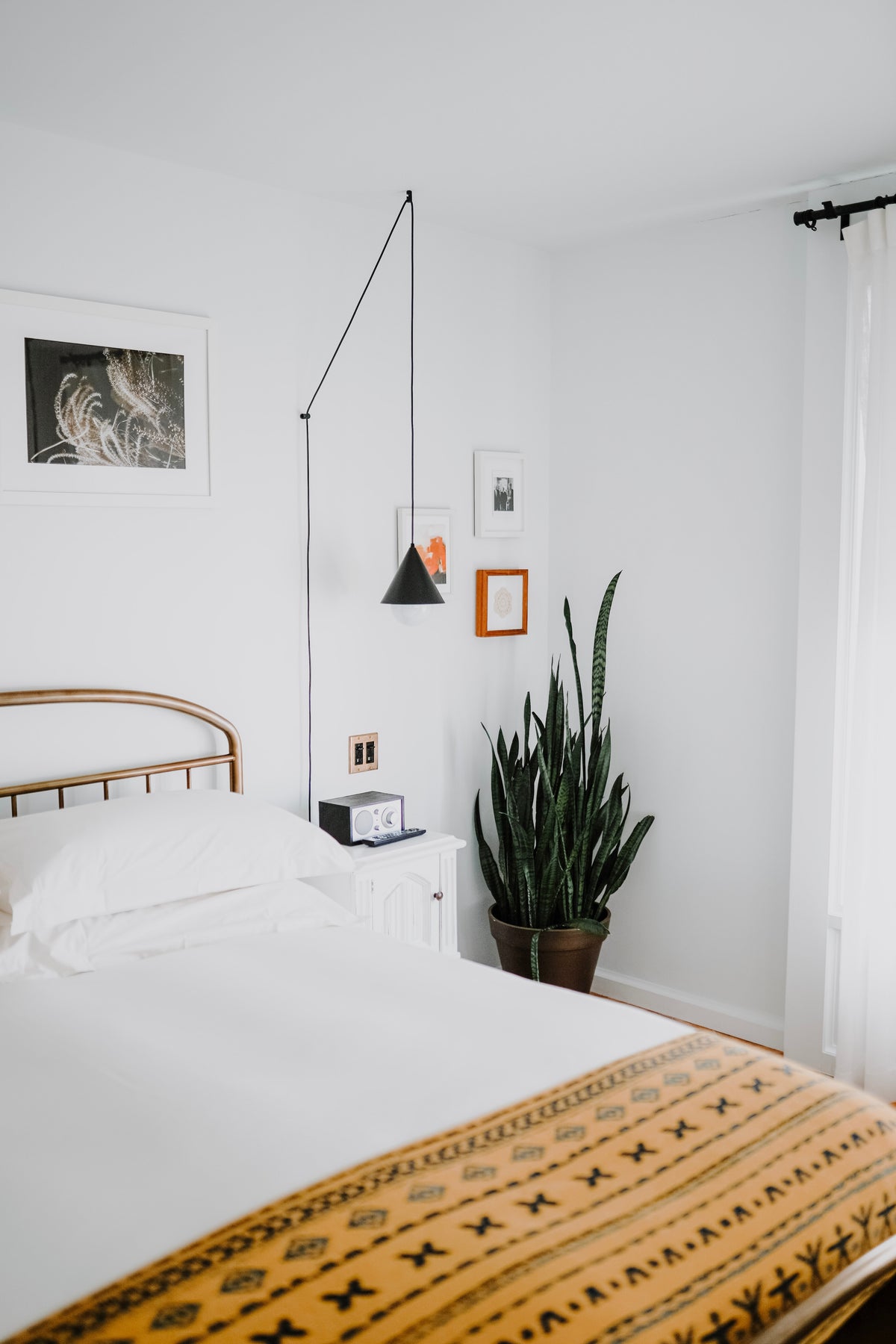 Ein minimalistisches Schlaf-Zimmer mit einer Sansevieria in der Ecke. Das Bett ist weiss, sowie auch der Nachttisch.