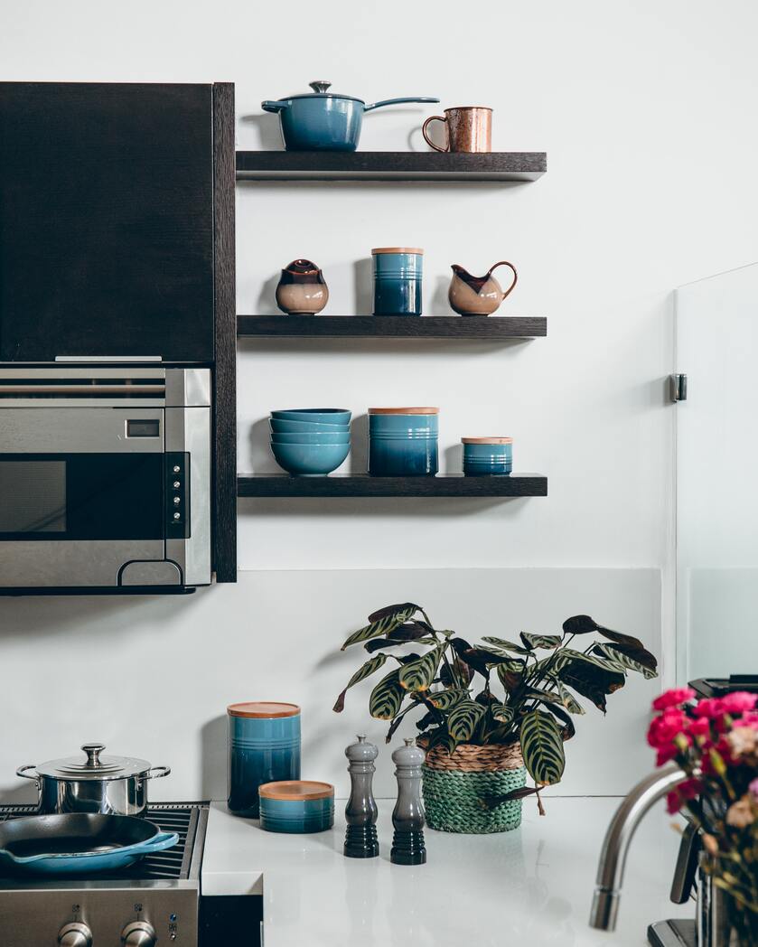 Blaues Keramikgeschirr auf braunen Küchenregalbrettern und weisser Arbeitsfläche, wo auch Pflanzen noch Platz finden