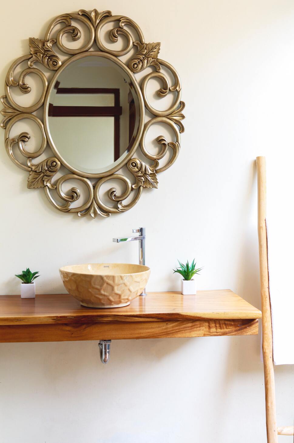 Spiegel mit goldenen Ornamenten, abgesetztes Waschbecken, rechts und links davon zwei kleine Pflanzen