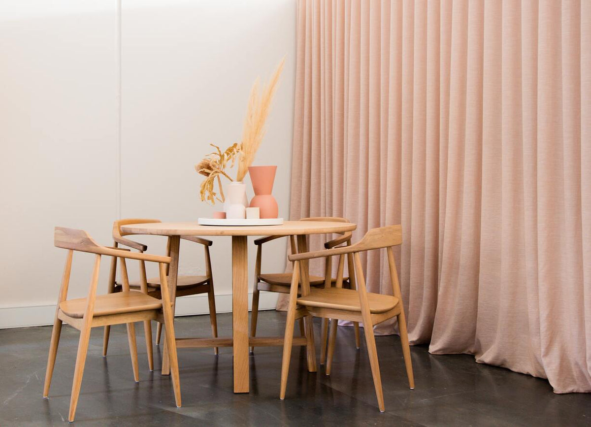 Trockenpflanzen in weisser und rosa Vase auf rundem Holztisch mit hölzernen Stühlen, dahinter ein pastellfarbener Vorhang