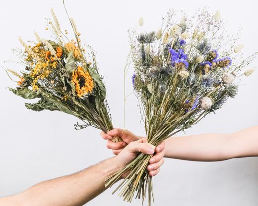 Zwei Hände, die Trockenblumensträusse halten und sich kreuzen