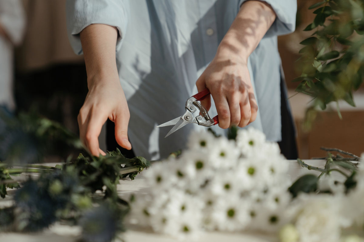 Frau in Hemd schneidet Blumensträusse und Pflanzenstängel mit einer Gartenschere