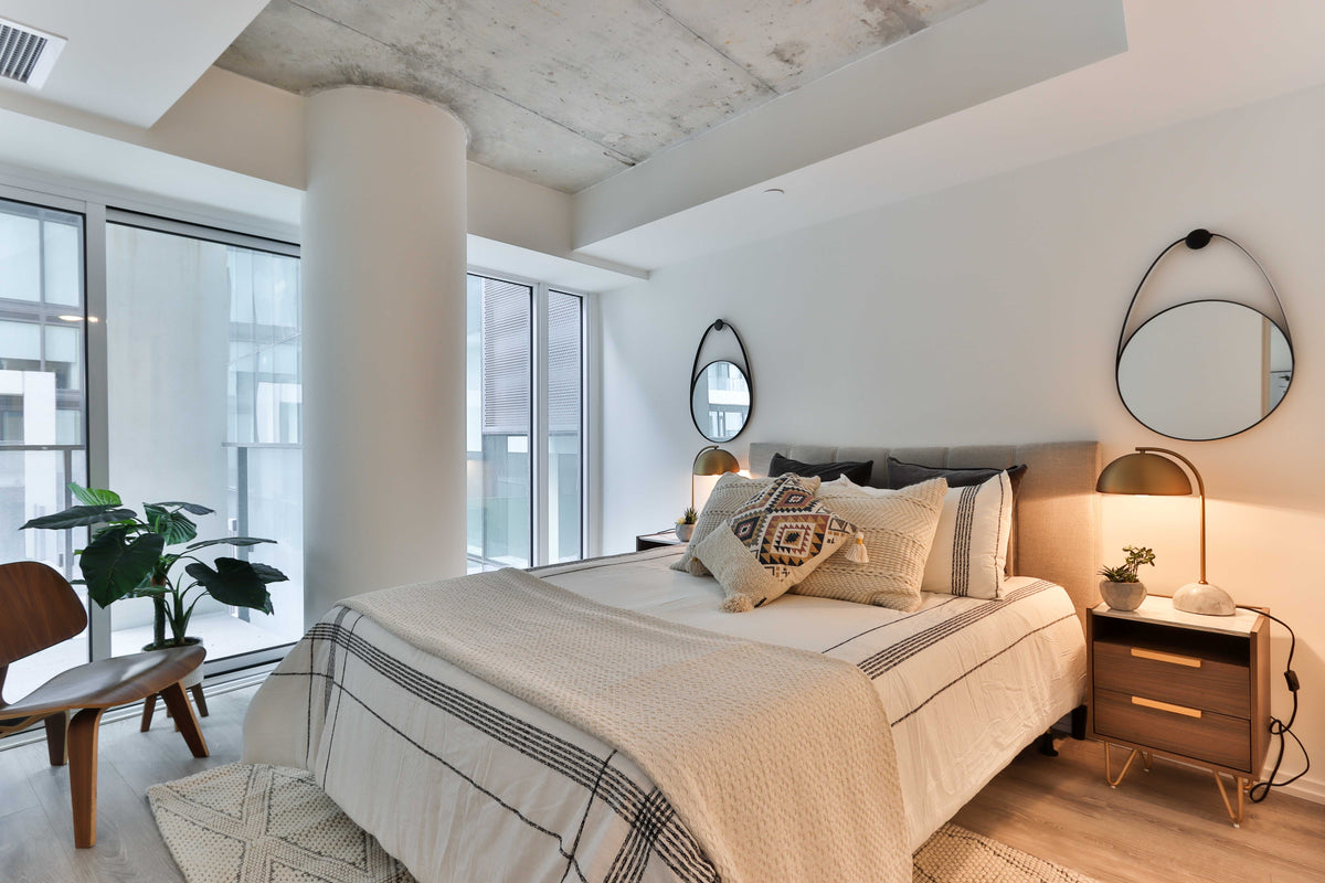 ein Schlafzimmer im skandinavischen Style mit Teppich, hellen Bettdecken, Holz-Nachttisch und zwei Spiegeln an der Wand.