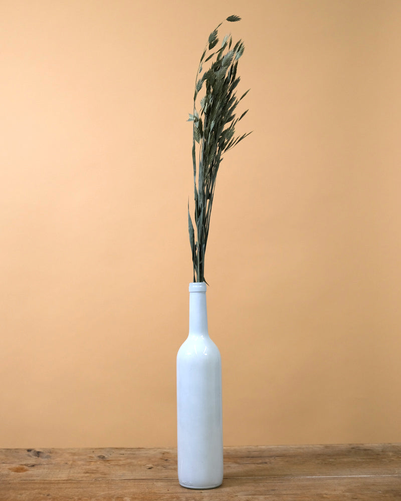 Bündel Trockenpflanzen in einer weissen Vase auf einem Holztisch