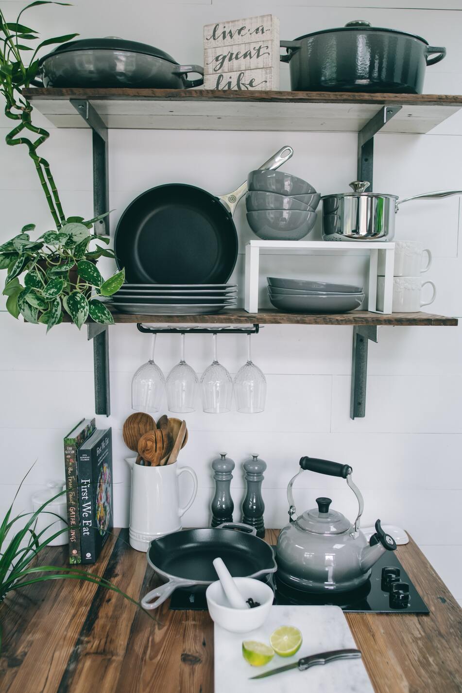 holzige Kücheninsel vor einer weissen Wand mit hölzernem Regal, darauf diverse Utensilien in grau, weiss und schwarz