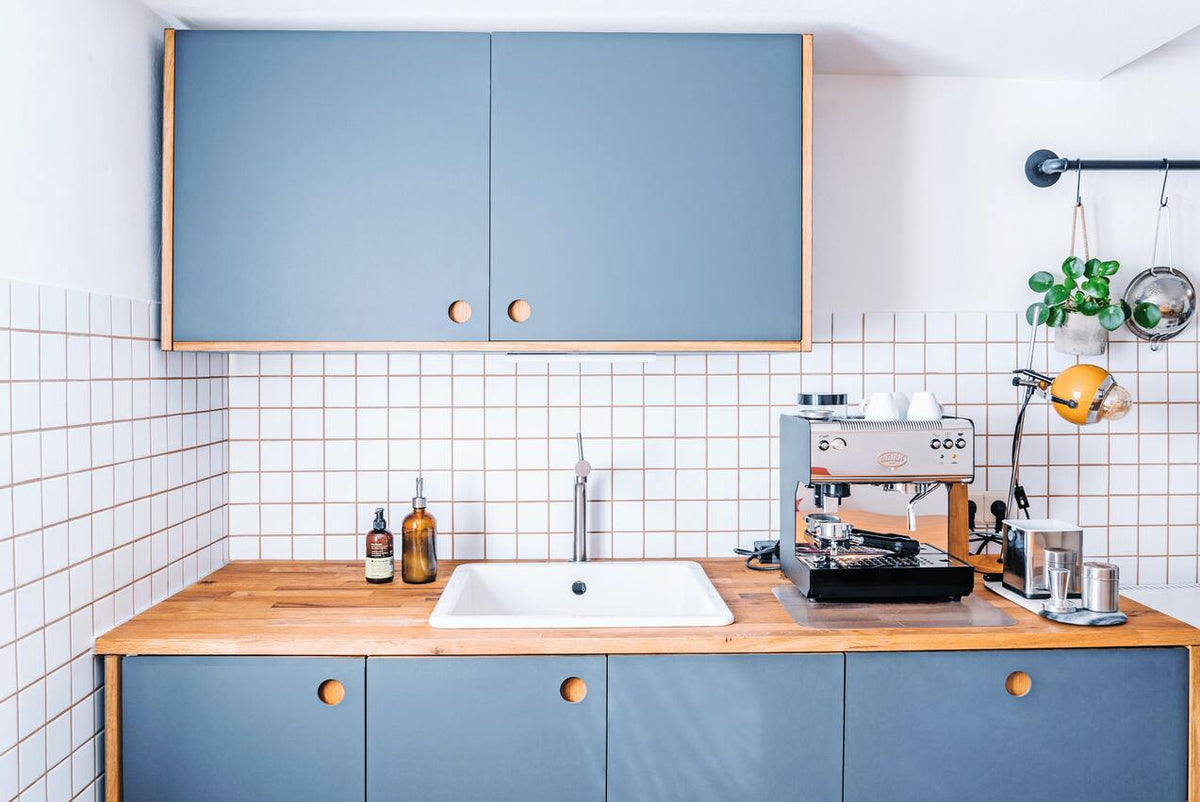 Blaue Küche mit Holzablagefläche, weisse Kacheln in der Küche und Hängepflanze im Leerraum