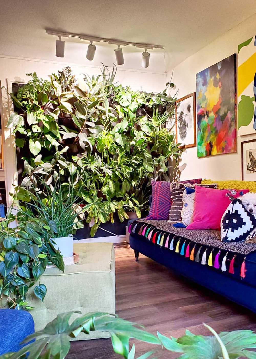 Pflanzenwand hinter einem violetten Sofa mit farbigen Kissen und einem bezogenen Couchtisch, auf dem ebenfalls Pflanzen stehen