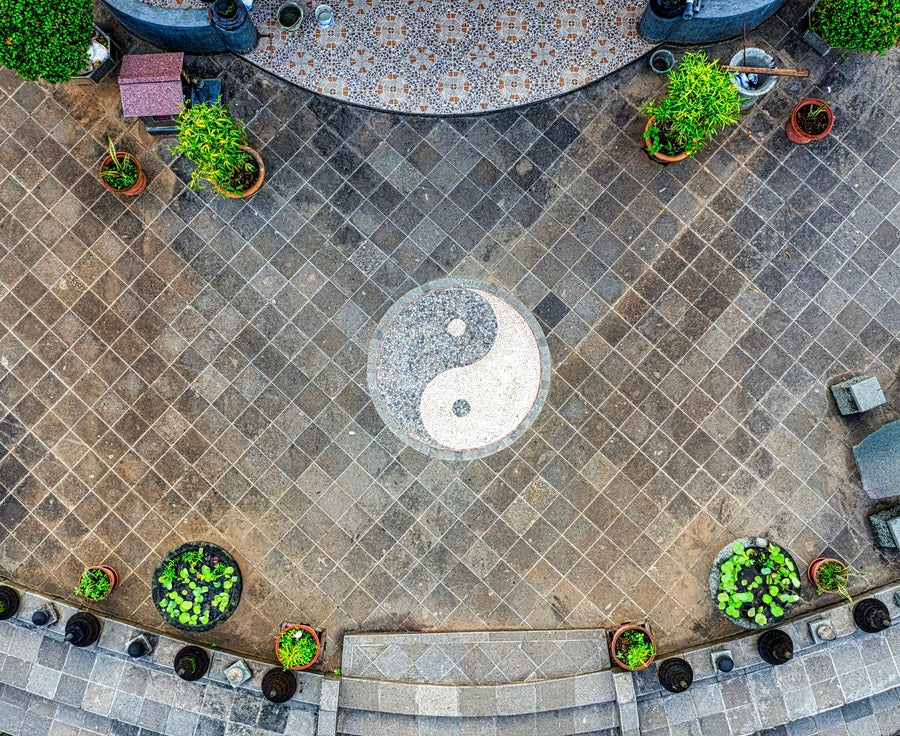 Plattenboden draussen mit einem Yin-Yang-Zeichen in der Mitte und einigen Aussenpflanzen am Rand platziert