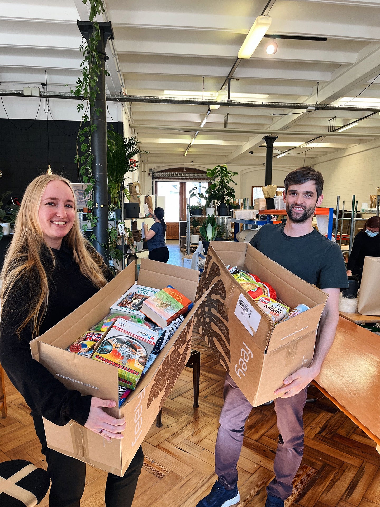 Jil Claire und Sven halten zwei Schachteln mit Spenden aus der Aktion «Zurücksenden und spenden»-Gütern.